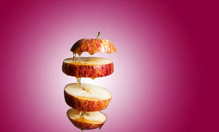Fresh sliced Red apple and honey dripping in flying food with levitation reflection. Alternative sugar substitute, cold remedy and body strengthening, superfood breakfast red background.の写真素材