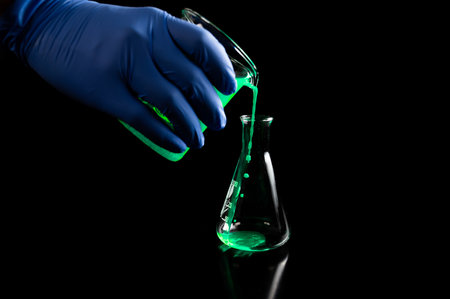 A woman scientist experimenting with a green fluorescent solution in a glass conical flask in dark...