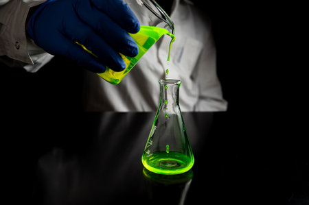 A research scientist experimenting with a green fluorescent droplets in a glass conical flask in dark biomedical laboratory for health care medicine development. Copy space black backgroundの写真素材