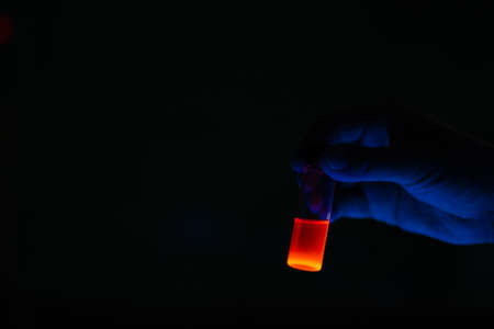 A woman researcher holding chemistry photochemical reaction fluorescent glass vials in a organic laboratory. A copy space black background. Medicinal chemistry laboratory.の写真素材