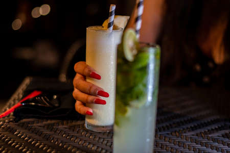 A happy woman holding cold cocktail glass with condensed water droplet during the evening in a...