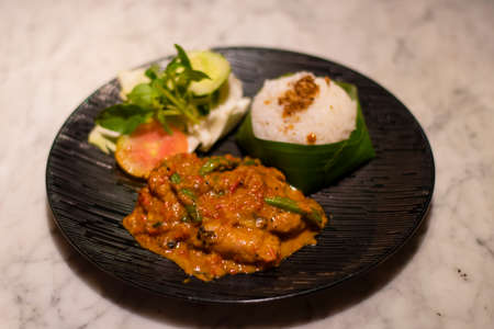 Decorated platter dinner with creamy chicken, rice and salad served in a black plate on a table in touristic visit in Bali, Indonesiaの写真素材