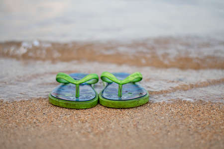 A pair of green slippers in a seaside touching the wave with sands in a tranquil exotic weather during the summer in Bali, Indonesiaの写真素材