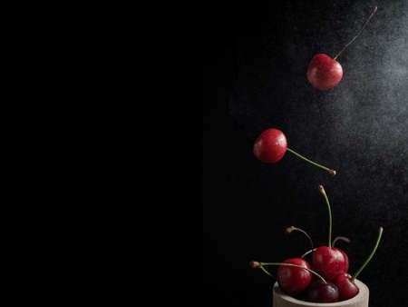 Collection of fresh cherries on a dark background, dynamic shot with action, splash, water drops and bokeh. Fresh fruit floating or levitating shotwith water droplet and dark background.の写真素材
