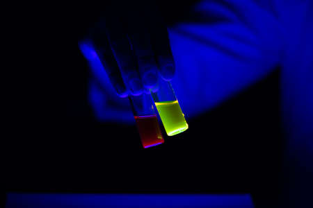 Toxic chemical sample glass vials hold by a woman scientist in a laboratory - radioactive - fluorescence. A black background.の写真素材