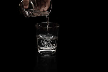 A kid is pouring water with curvy flow in a clear glass with bubble formation for saving water and sustainability of the earth concept in a dark backgroungの写真素材