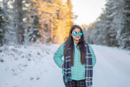 Portrait of a beautiful woman dressed with colourful jacket. A beautiful woman in coloured jacket walking through the Magical winter forest. Natural landscape with cloudy sky.の写真素材