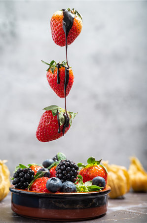 Dipping dark chocolate on flying strawberry into pot with chocolate on white marble background. Copy space isolatedの写真素材