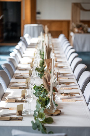 Wedding decor. Beautiful event venue. Indoor round reception table with flowers and chairs. Compositions of flowers and plants in  wooden stands.の写真素材