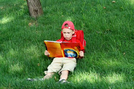 The boy during a school vacation has a rest in a wood reading the bookの写真素材