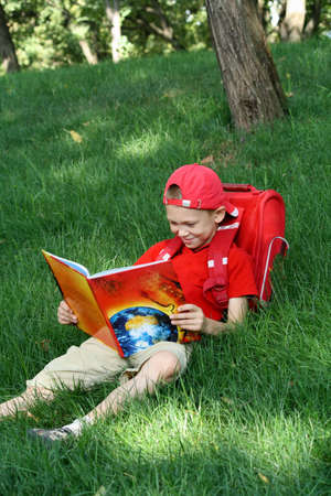 The boy during a school vacation has a rest in a wood reading the bookの写真素材