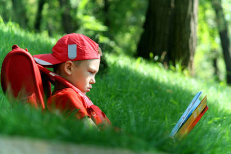 The boy during a school vacation has a rest in a wood reading the bookの写真素材