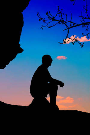 Silhouette of a man sitting at sunset skylineの写真素材