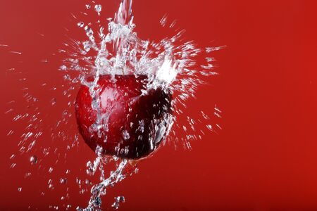 red apple under a waterfall splashing on a red backgroundの写真素材
