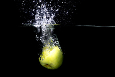 Green apple falling in water with splash on black background.の写真素材