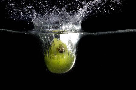 Green apple falling in water with splash on black backgroundの写真素材