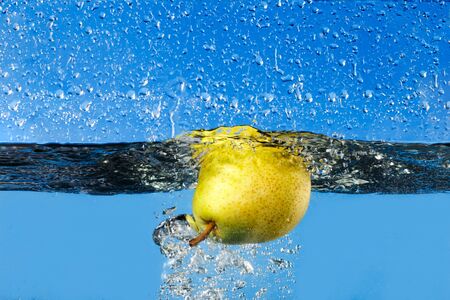 fresh pear dropping into water on blue backgroundの写真素材