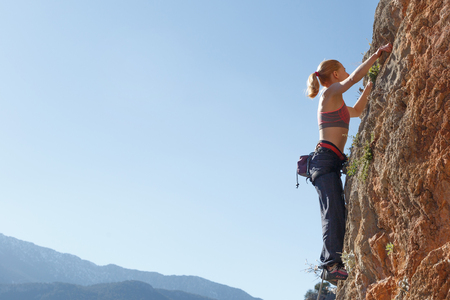 A young girl climber climbs high up the cliff in Geyikbayiri Turkey. Against the background of the skyの写真素材