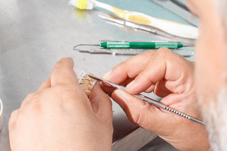 Dental prosthesis, dentures, prosthetics work. Prosthetics hands while working on the denture, false teeth, a study and a table with dental tools.の写真素材