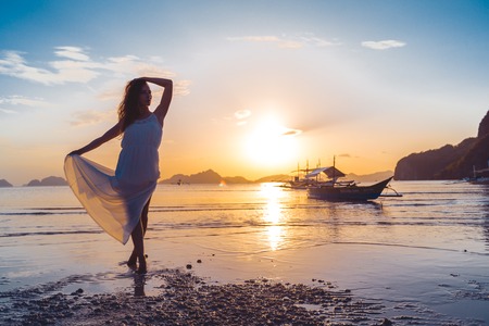A woman in a white dress at sunset on the background of a traditional Filipino boat. El Nido, Plawan island, Philippineの写真素材