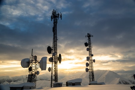 Communication tower with antennas and satellite dishes at background of a winter mountain landscape,...