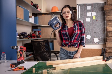 Home diy woman cutting plank of wood on workbench with saw renovating improving and decorating homeの写真素材