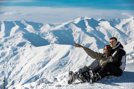 young couple in the snow, the girl shows a finger to the side. Ski resort, winter holidaysの写真素材