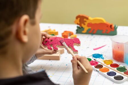Rear view of a child, hands decorate a wooden toy with a watercolor brush