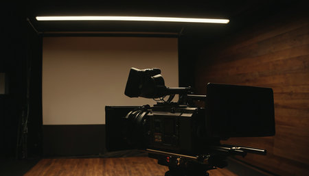 Video camera on a tripod in a dark room with lights on.の素材