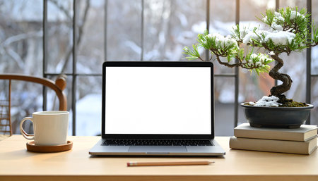 Mockup image of laptop with blank white screen on wooden desktop with coffee cup and bonsai tree in the backgroundの素材