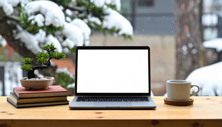 Mockup image of laptop with blank white screen on wooden table with books, coffee cup and bonsai tree in snowfallの素材