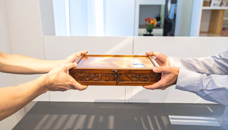 Man and woman hands holding wooden casket in the living room.の素材