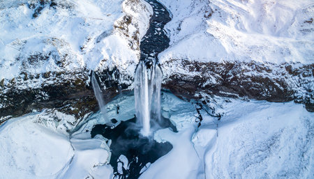 An overhead drone view of a waterfall in a snow-covered mountainous landscape. Clear details and vibrant colors enhan...の素材