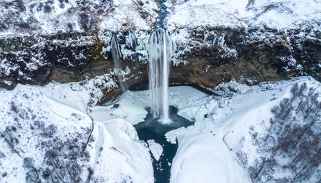 Aerial perspective of Seljalandsfoss waterfall in Iceland during winter with ice and snow creating a frozen spectacle.の素材