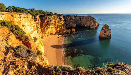 A secluded golden sand beach nestled between Algarve Portugal's sunlit cliffs with clear turquoise water.の素材