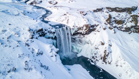 An aerial perspective of the majestic Skogafoss waterfall in Iceland, heavily covered in snow and ice during winter.の素材