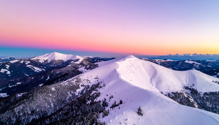Aerial view of snow-capped mountains with a soft pink and purple gradient sunset skyの素材