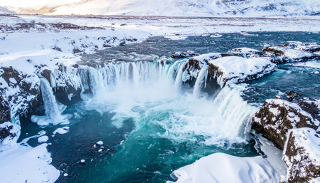 A wide aerial view of a powerful waterfall in Iceland surrounded by snow and ice during winter.の素材