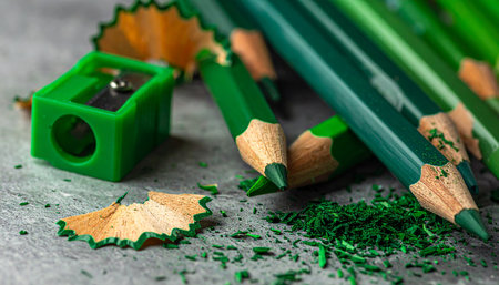 Green colored pencils, sharpener, and wood shavings on a gray concrete surface. Clear details and vibrant colors enha...の素材