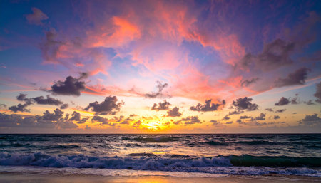 A colorful sunset with breaking waves on a sandy beach is framed by textured clouds in the sky.の素材