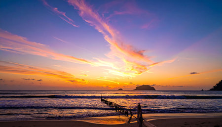 A dramatic sunset illuminates the sky with colorful clouds over the ocean and a weathered wooden pier.の素材