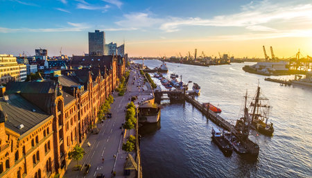 Hamburg harbor at sunset with historic brick warehouses, boats, and industrial cranes.の素材