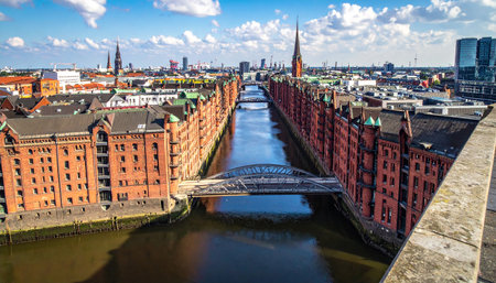 Aerial view of Hamburg Speicherstadt with canals, bridges, and historic brick warehouses under a blue sky.の素材