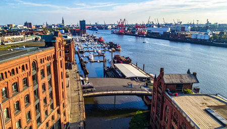 Hamburg harbor with historic Speicherstadt warehouses, a marina full of boats, and industrial cranesの素材