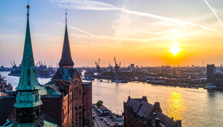 Hamburg harbor at sunset with historic Speicherstadt buildings and industrial cranes visibleの素材