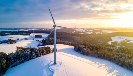 Snowy landscape with wind turbines at sunset with golden light and clouds in the skyの素材