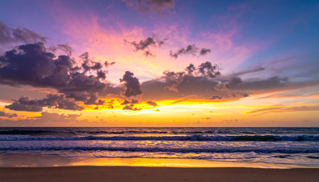 A vibrant sunset paints the sky with orange, yellow, and purple hues over a calm ocean with gentle waves.の素材