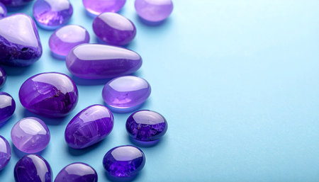 Smooth polished purple amethyst gemstones scattered across a light blue surface with copy spaceの素材