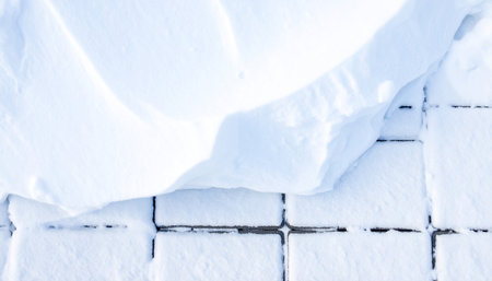 A large, soft drift of snow partially covers a pattern of rectangular paving stones.の素材