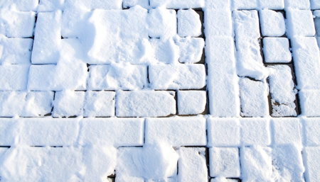 Overhead view of paving stones with uneven snow coverage creating a textured winter ground surface.の素材